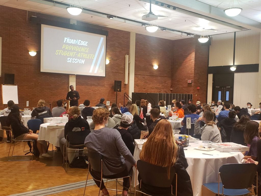 First year student-athletes seated at round tables of 8, engage in dialogue with Dr. Collin Williams Jr. from Rise